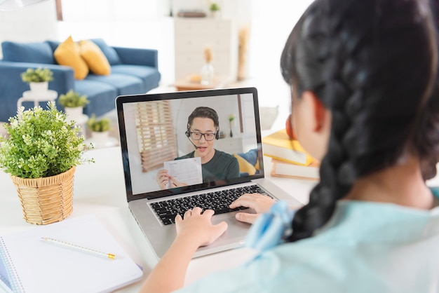 Homeschool Asian little young girl student learning virtual internet online class on table at home. distance online learning concept. protect from COVID-19 viruses.