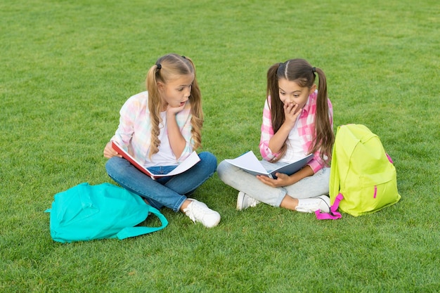 Do homework together find something interesting in book making notes spend free time after school small kid friends relax on grass back to school literature for girls