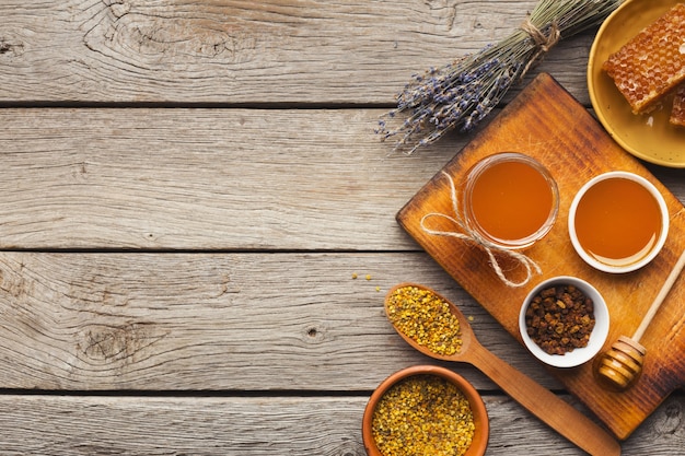 Honey assortment on rustic wood. Top view on full glass jars, honeycombs, pollen bowl, nuts, ginger, mint and dry oranges. Sweet background, wallpaper. Natural medicine concept, copy space