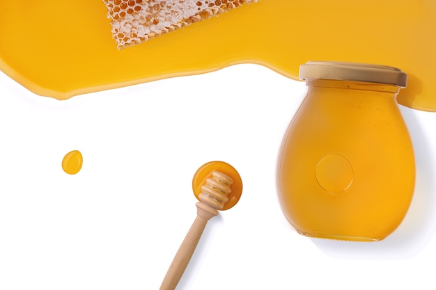 Honey background. Sweet honey in the comb, glass jar and a spoon for honey on the table. White background. Top view.