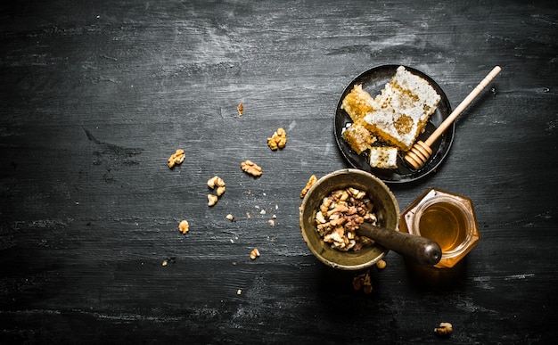 Honey background . Walnuts in a mortar and sweet honey in the comb. On black rustic table.