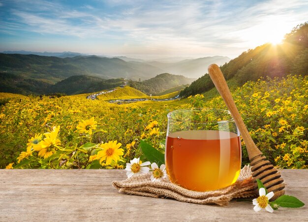 Honey Bee in glass jar with honey dipper and flowers on the wooden table flower garden background at sunrise or sunset