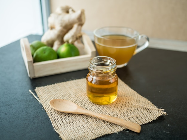 Honey bottle on sack and on wooden black background, blur lemon and water ginger background,