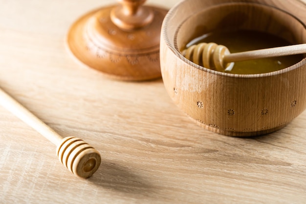 honey in a deep wooden bowl, rustic wooden plate. The wooden spoon drips slowly.