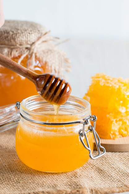 Honey dripping from a wooden honey dipper in a jar on wooden grey rustic