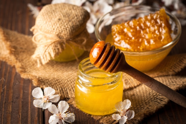 Honey dripping from a wooden honey dipper in a jar on wooden grey rustic 