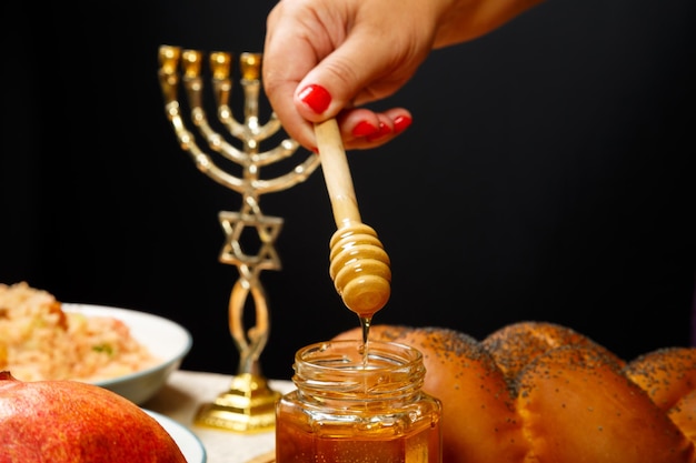 Honey drips from a wooden spoon in a woman's hand next to the menorah challah and couscous and pomegranate