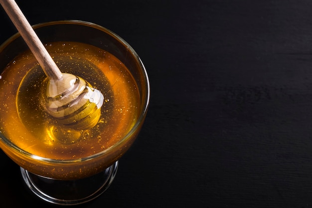 Honey in a glass bowl with honey dipper on a dark. Sweet golden honey. Space for text. Top view