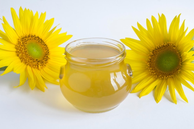 Honey in the glass jar and sunflower on the white background Closeup