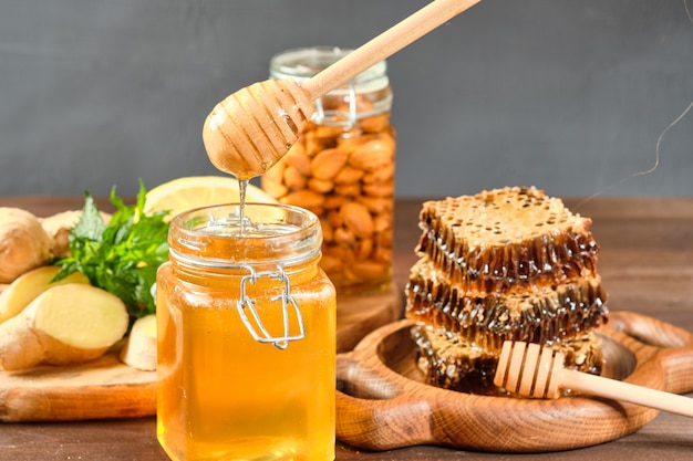 Honey in honeycombs on a wooden plate and golden honey in a jar with nuts and comb for honey with lemon and ginger