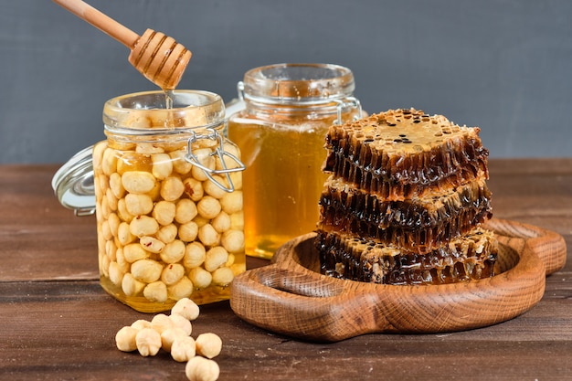 Honey in honeycombs on a wooden plate and golden honey in jars with nuts