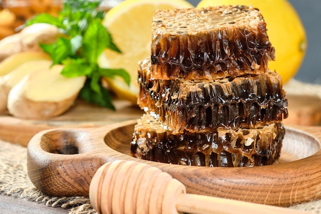 Honey in honeycombs on a wooden plate and honey with nuts with lemon and ginger in rustic style on a wooden table.