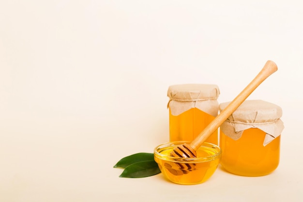 Honey in jar with leaves and honey dipper on colored background top view with copy text