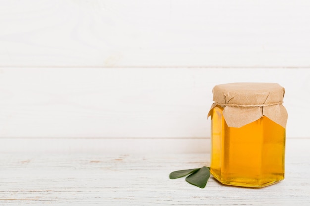 Honey in jar with leaves and honey dipper on colored background top view with copy text