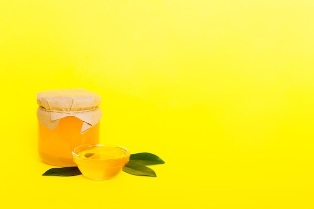 Honey in jar with leaves and honey dipper on colored background top view with copy text