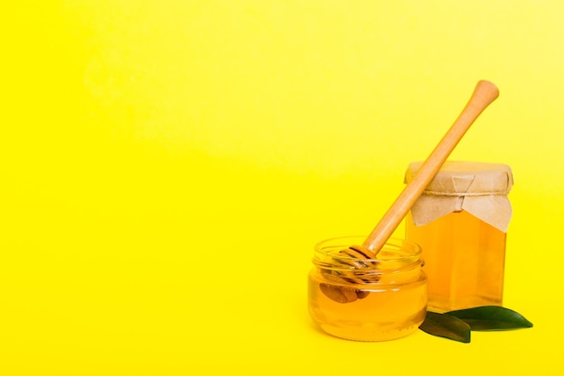 Honey in jar with leaves and honey dipper on colored background top view with copy text