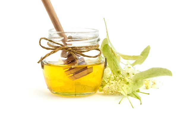 Honey jar with linden blossom and wooden honey dipper isolated on white background