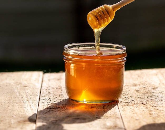 Honey jar on wooden table and dark backgroun honey dripping from honey dipper