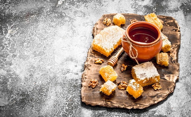 Honey pot and honeycomb with nuts. On rustic table.