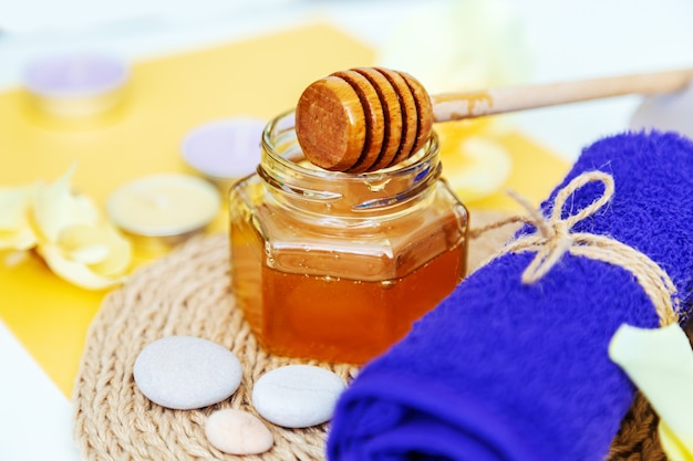 Honey spa treatment. Gold honey in a jar, orchid flowers, towels and scented candles. Natural home skin care. Yellow background.