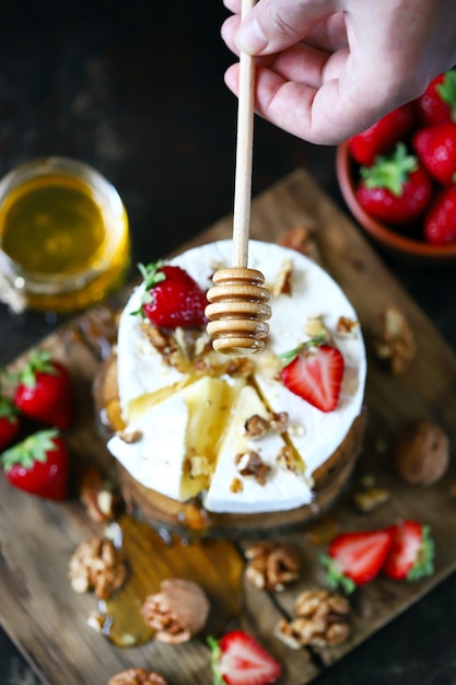 A honey stick pours honey on a Camembert