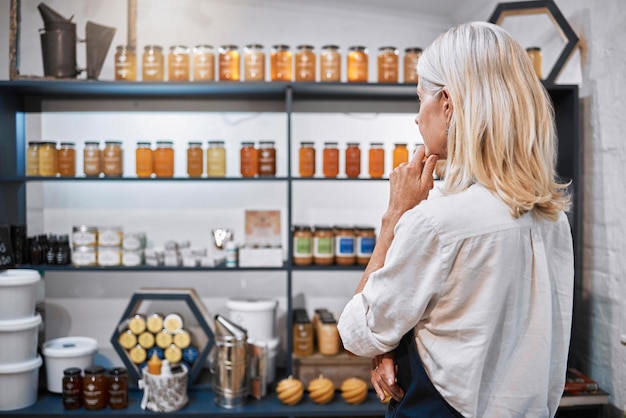 Honey store owner grocery shop or woman thinking on shelf ideas sales product price or stock management Mature small business or organic supermarket worker planning bee syrup container promotion