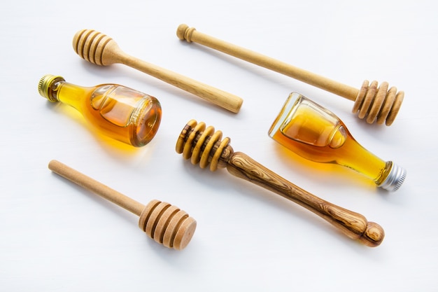 Honey wooden dipper and little honey bottle on white wooden background.