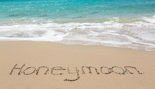 Honeymoon written in sand with sea surf