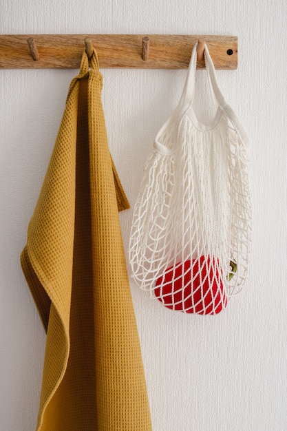 Hook hanger with white eco bag with a bell pepper and a yellow cotton towel,  hanging on a white wall in the modern kitchen