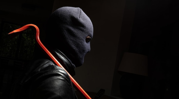 Hooligan in balaclava holding a crowbar black background