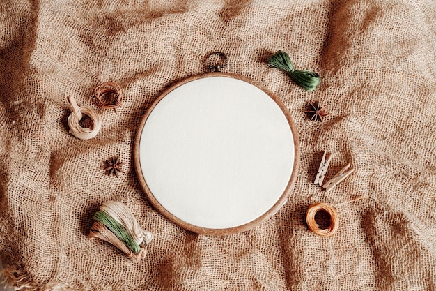 Hoop with white cotton fabric and threads on the background of burlap