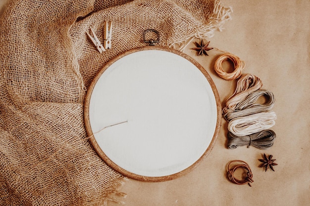 Hoop with white cotton fabric and threads on the background of burlap