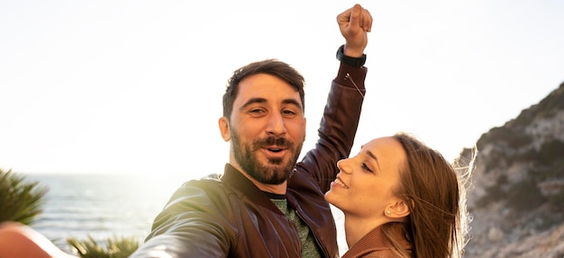 Horizontal banner or header with hipster young couple having fun taking a selfie portrait against a beautiful panorama at sunset Boyfriend and girlfriend in love smiling at the camera together