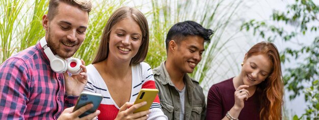 Horizontal banner or header with multicultural friends having fun together looking at their smartphones at dehor garden on college campus People addicted by mobile smart phones