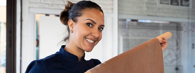 Horizontal banner or header with young beautiful smiling woman showing a big rolling pin with brown homemade sfoglia with semolina and cocoa Middle Eastern Sfoglina making fresh home made pasta