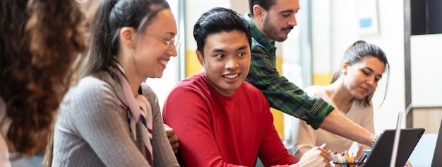 Horizontal banner or header with young coworkers multiethnic team planning a new startup People working on a new project in creative coworking office Bright filter with focus on asian man face