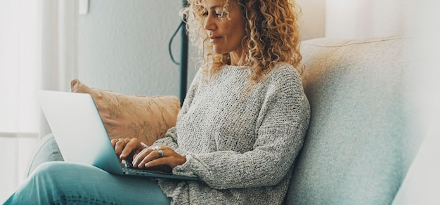 Horizontal banner image with young mature woman using laptop sitting on the sofa Concept of surfing the web people Modern female working on computer at home in relax time Lady use notebook happy