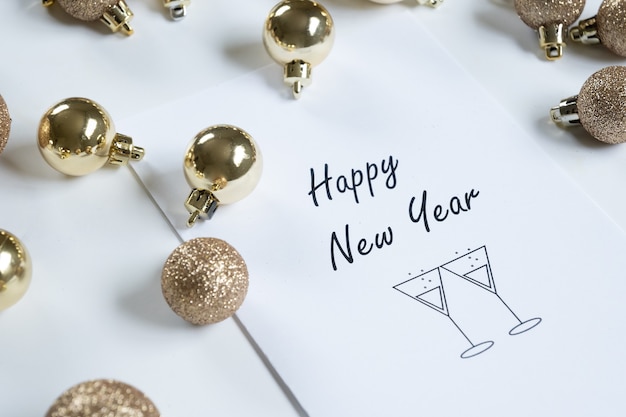 Horizontal close-up of "happy new year" card surrounded by golden Christmas balls, white background and copy space.