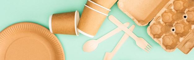 Horizontal crop of disposable tableware and wooden cutlery on green background ecology concept