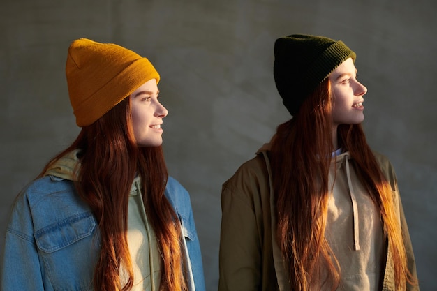 Horizontal medium portrait shot of two young women with long red hair wearing casual clothes and caps looking away smiling