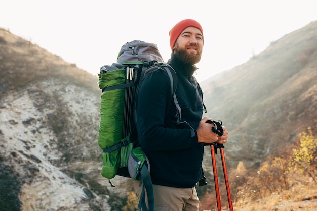 Horizontal outdoors portrait of hiker young male hiking in mountains with travel backpack Traveler man with beard trekking and mountaineering Travel people healthy lifestyle concept