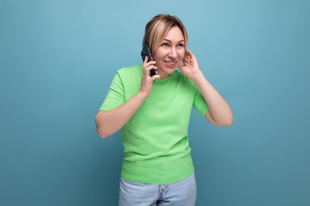 Horizontal photo of an adorable blond woman with a smartphone in her hands on a blue background with