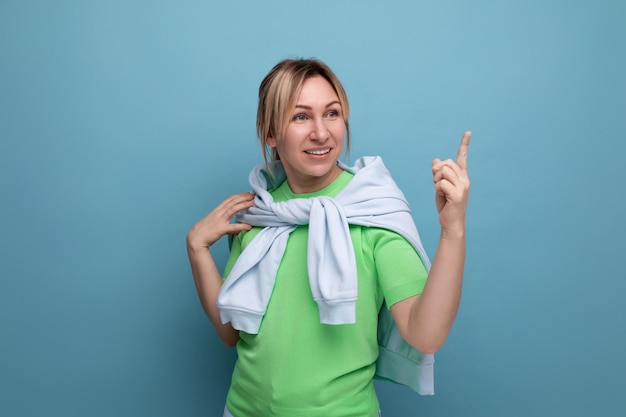 Horizontal photo of a blond positive bright girl in a casual outfit on a blue background with copy