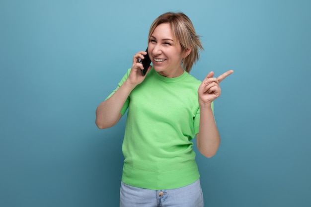 Horizontal photo of a cheerful joyful adorable blond woman with a smartphone in her hands on a blue