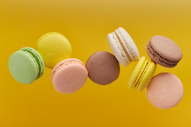 Horizontal photo of macaroon. Colorful cake macaron with pastel tones in chaotic levitation on an yellow surface. Top view of almond cookies.