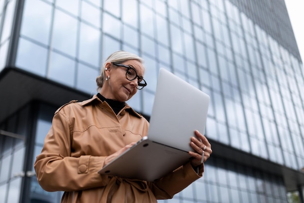 Horizontal photo of successful mature adult woman boss with laptop on building background