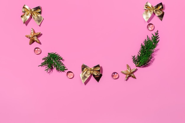 Horizontal pink festive background, copy space. Christmas decorations are laid out in the shape of a semicircle: golden bows, branches, straw stars, crystals