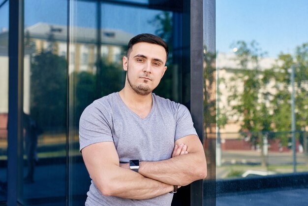 Horizontal portrait of athletic brunette guy in gray tshirt with folded hands looking at camera