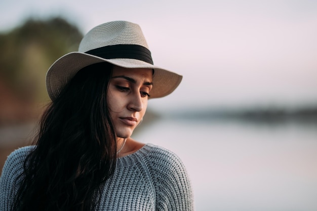 Horizontal portrait of a pensive and serious woman with her eyes closed wearing a hat by a lake