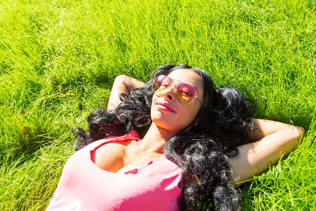 Horizontal portrait of pretty student girl spending day in park and showing thumb up Cheerful young female enjoying time in country Weekend and holiday concept